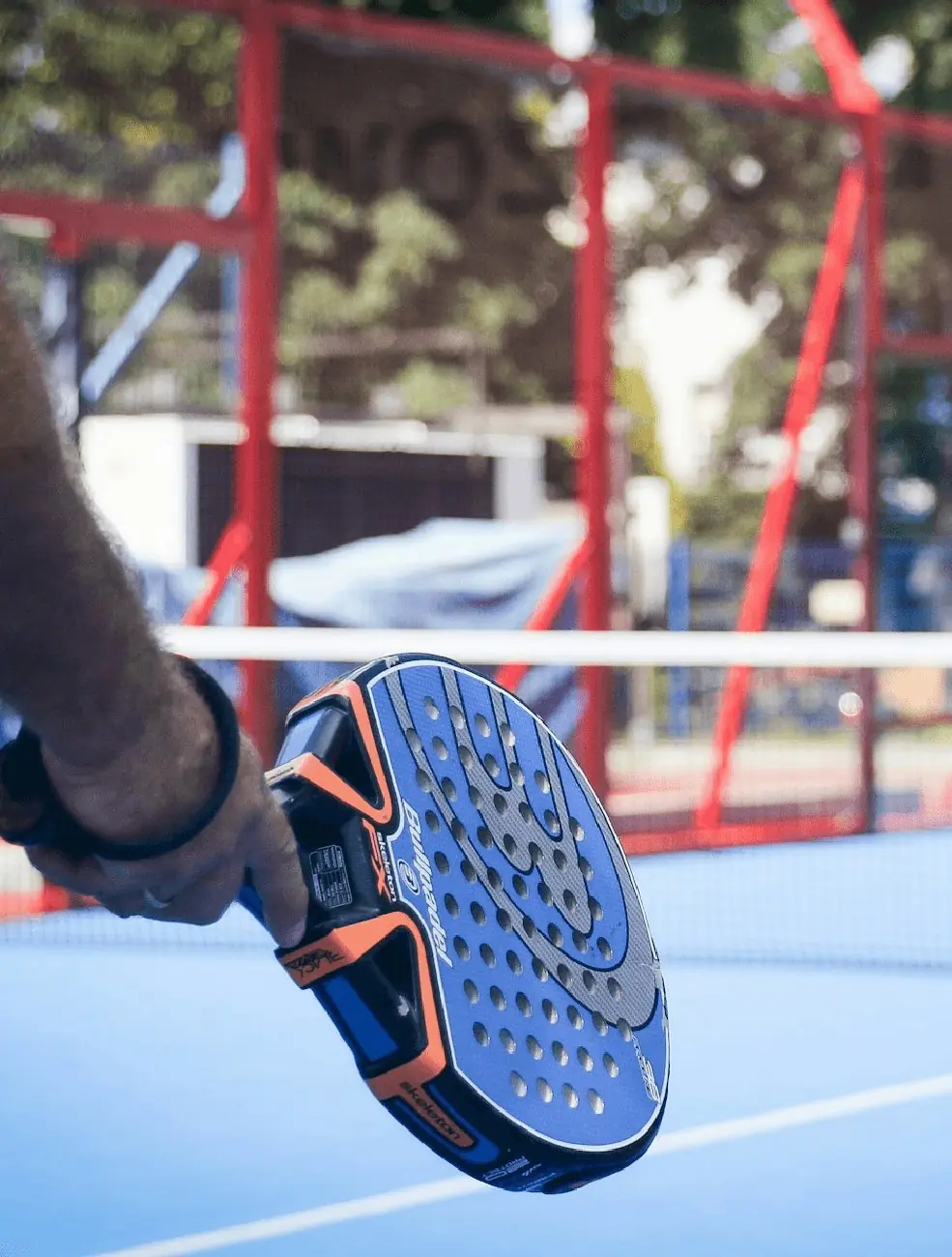 A padel racket in a player's hand at the net, close up.