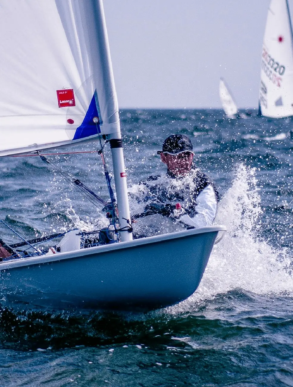 A dinghy sailor hiking out through the spray on open water.